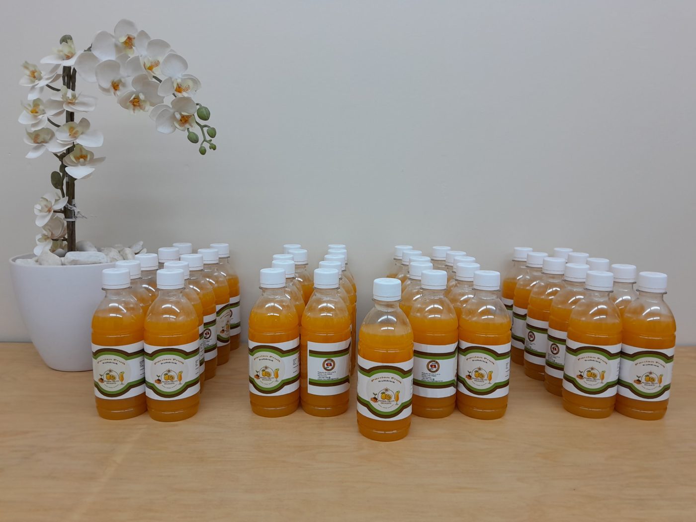 Rows of 350 ml Passion Fruity Delights fruit drink bottles beside an orchid
